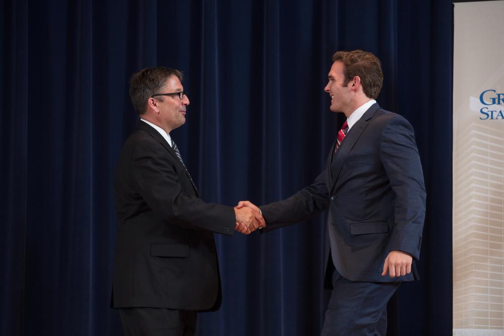 Doctor Smart shaking hands with an award recipeint in a grey suit and red tie